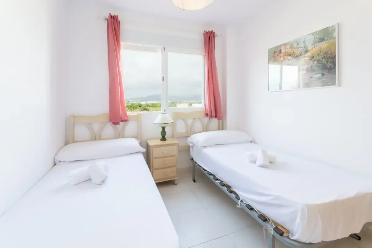 A bright bedroom with two beds and a window framed by pink curtains.