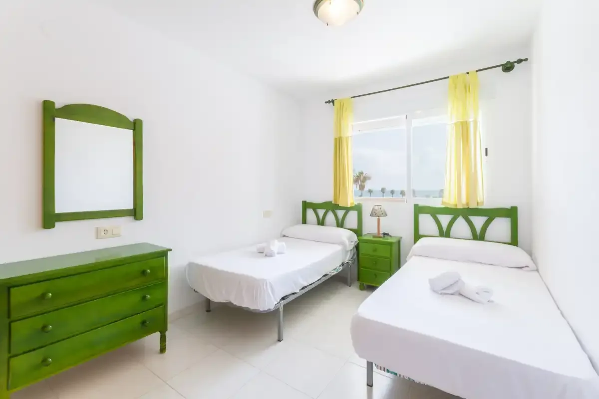 A bright bedroom with two beds, green furniture, and yellow curtains.