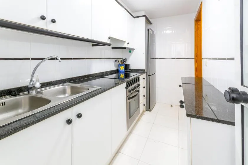 A bright kitchen with white cabinets, a double sink, and a built-in oven.