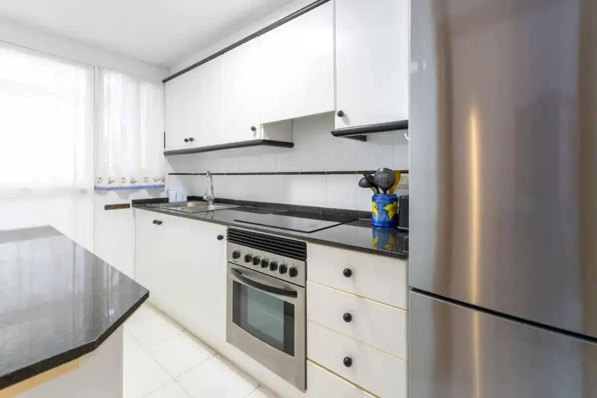 A bright kitchen with white cabinets, dark countertops, and a stainless steel refrigerator.