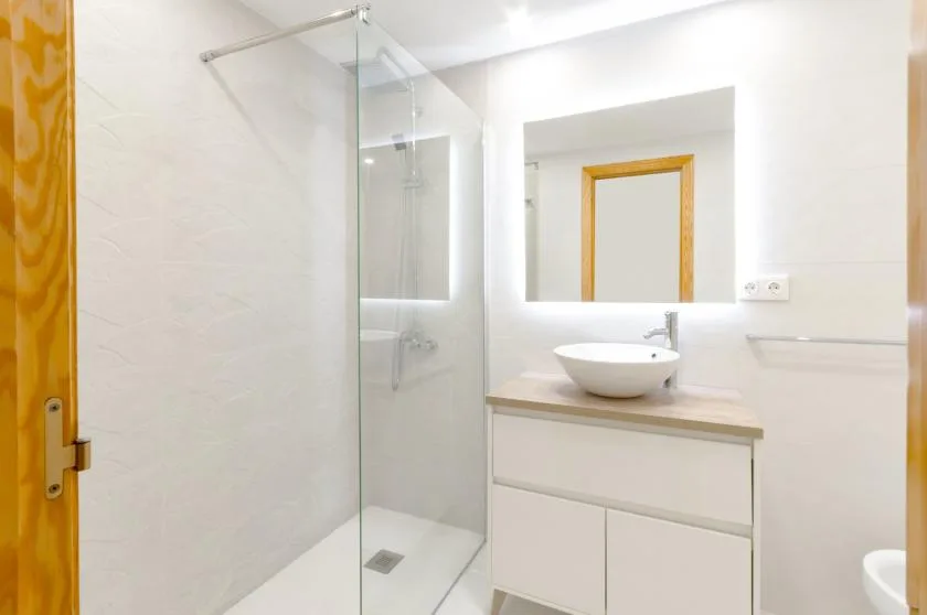 A bright bathroom with a glass shower and a sink beneath a mirror.