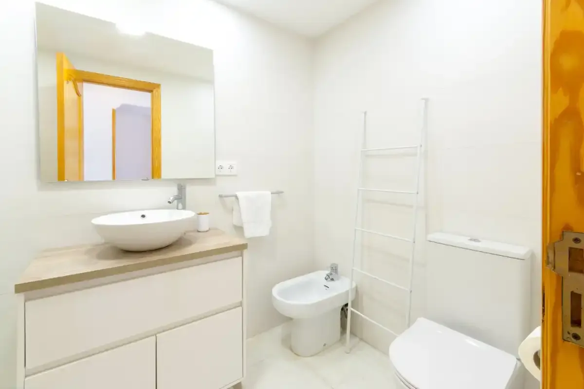 A bright bathroom with a sink, bidet, and white tiled walls.