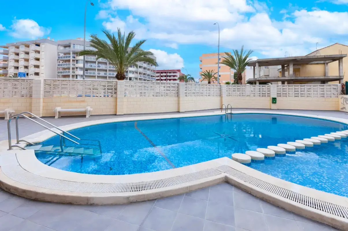An outdoor swimming pool sits beside a tiled deck and palm trees.