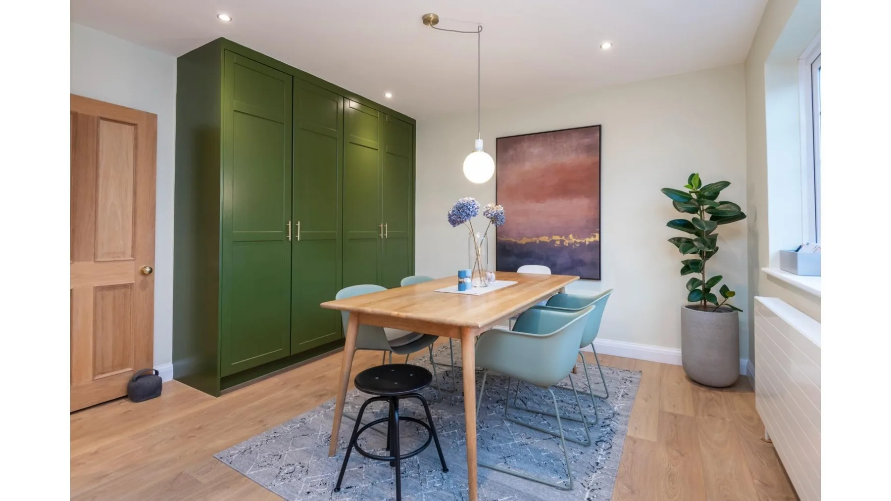 Un comedor con una mesa de madera, asientos azules y armarios verdes.