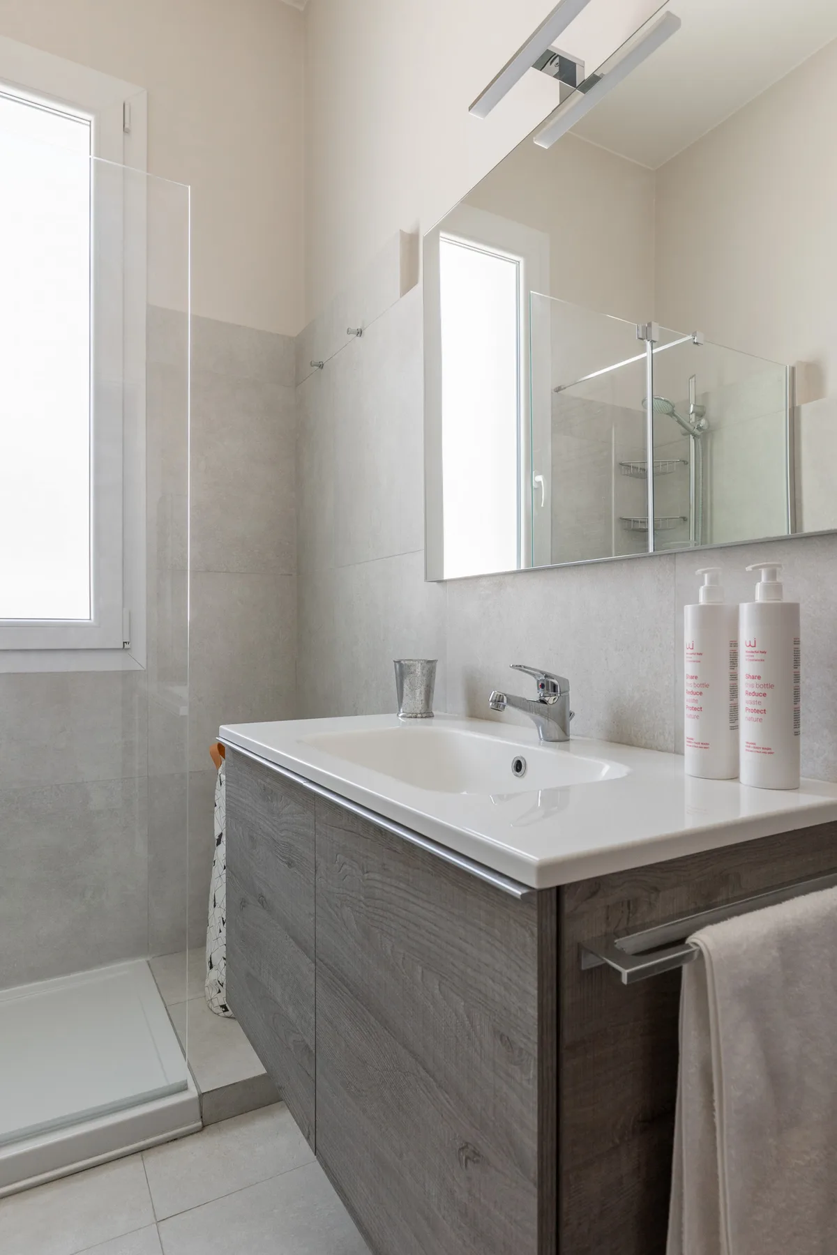 Baño luminoso con mueble de lavabo, espejo y ducha de vidrio.