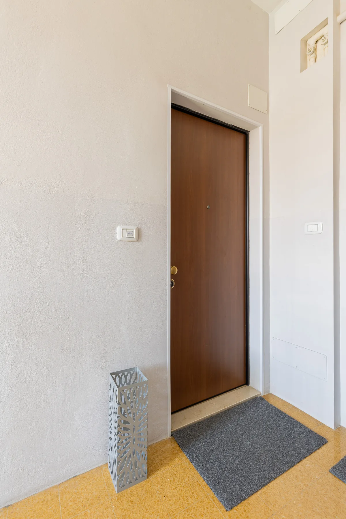 Una entrada interior con una puerta marrón y un felpudo oscuro.