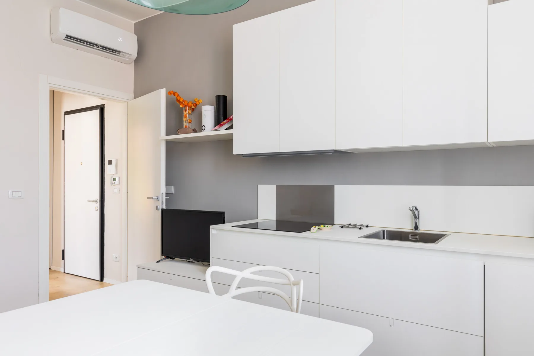 Una pequeña cocina luminosa con armarios blancos, fregadero y mesa de comedor.