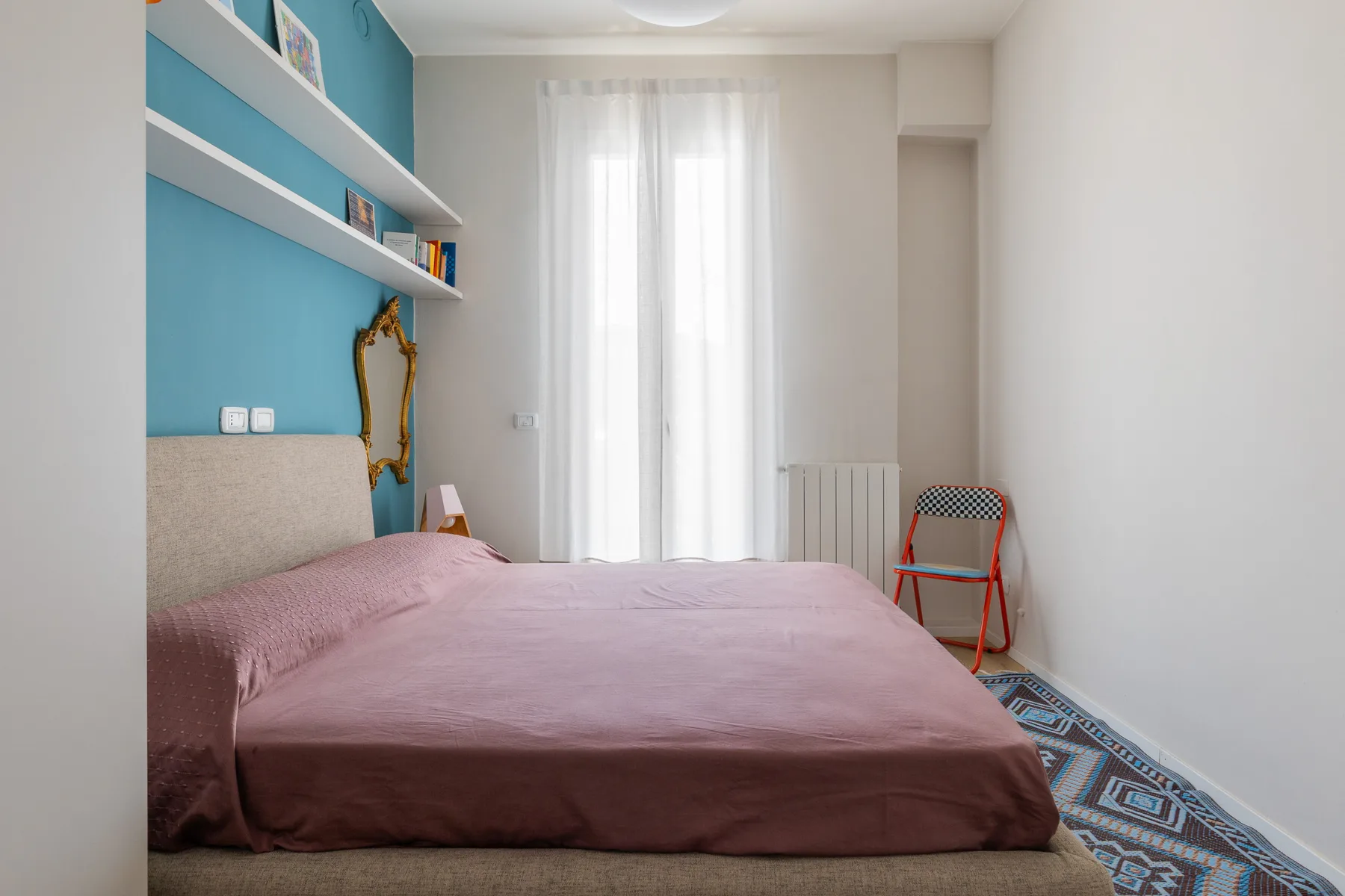 Un dormitorio con una cama junto a una ventana con cortinas claras.
