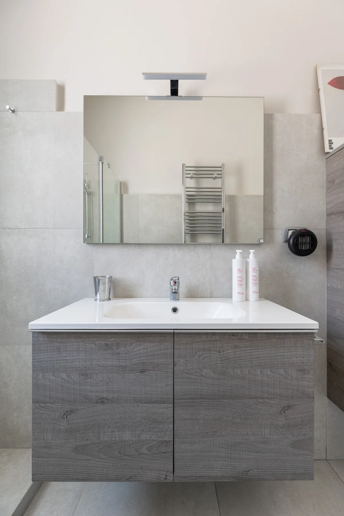 Un mueble de baño con un espejo amplio y un gabinete gris con acabado de madera.