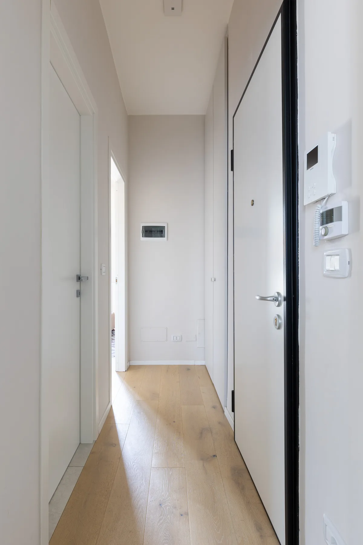 Un pasillo luminoso con suelo de madera clara y puertas blancas.