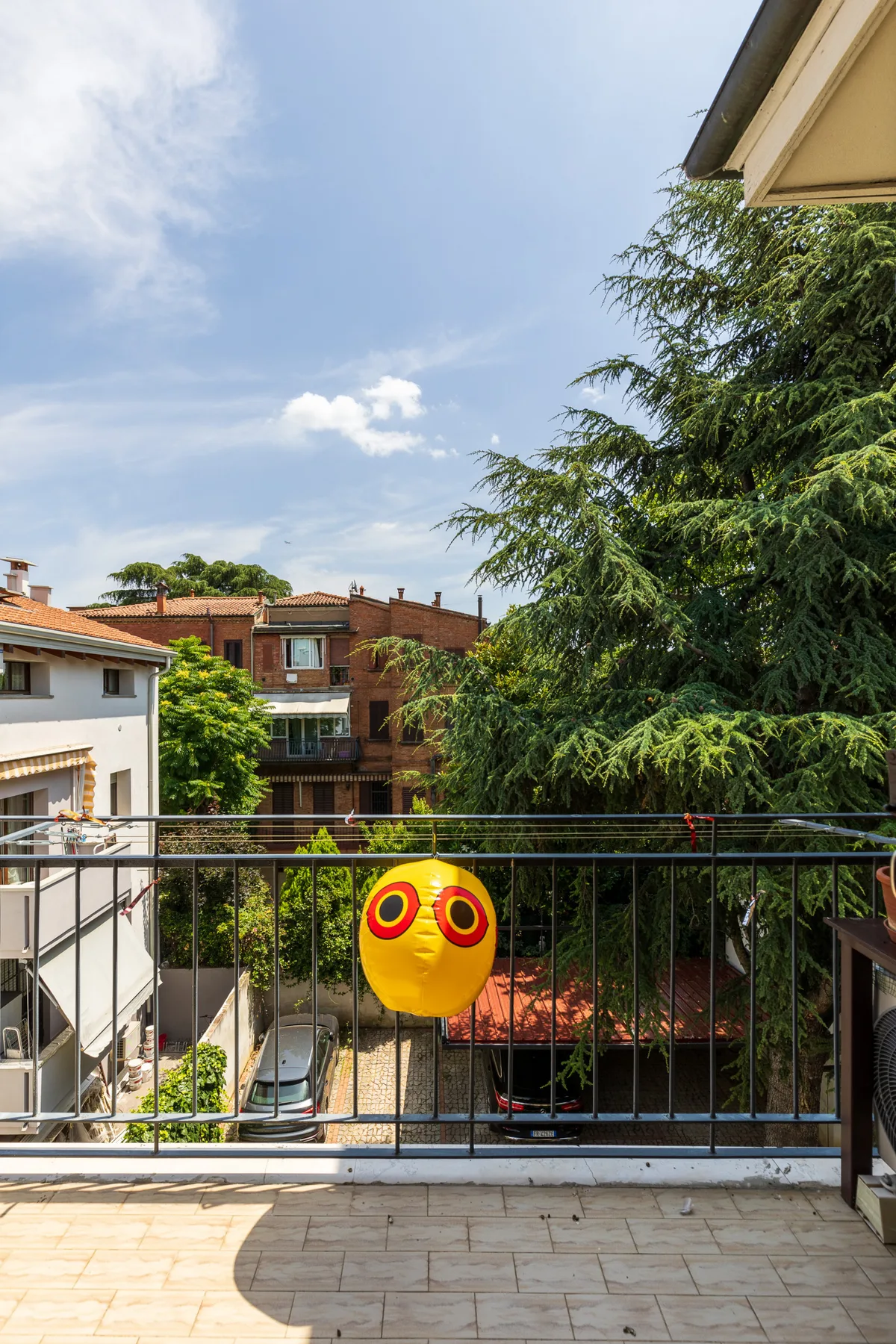 Un balcón soleado da a árboles frondosos y edificios residenciales cercanos.
