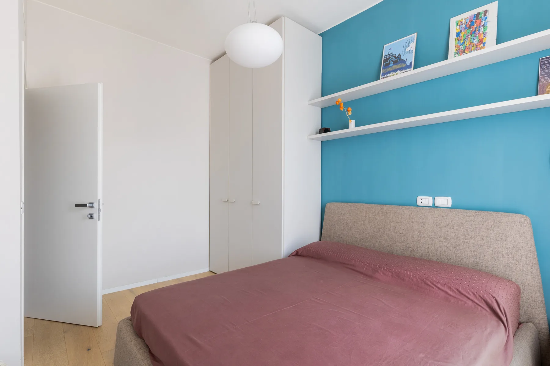 Un dormitorio con una cama bajo estantes de pared y una pared de acento color turquesa.