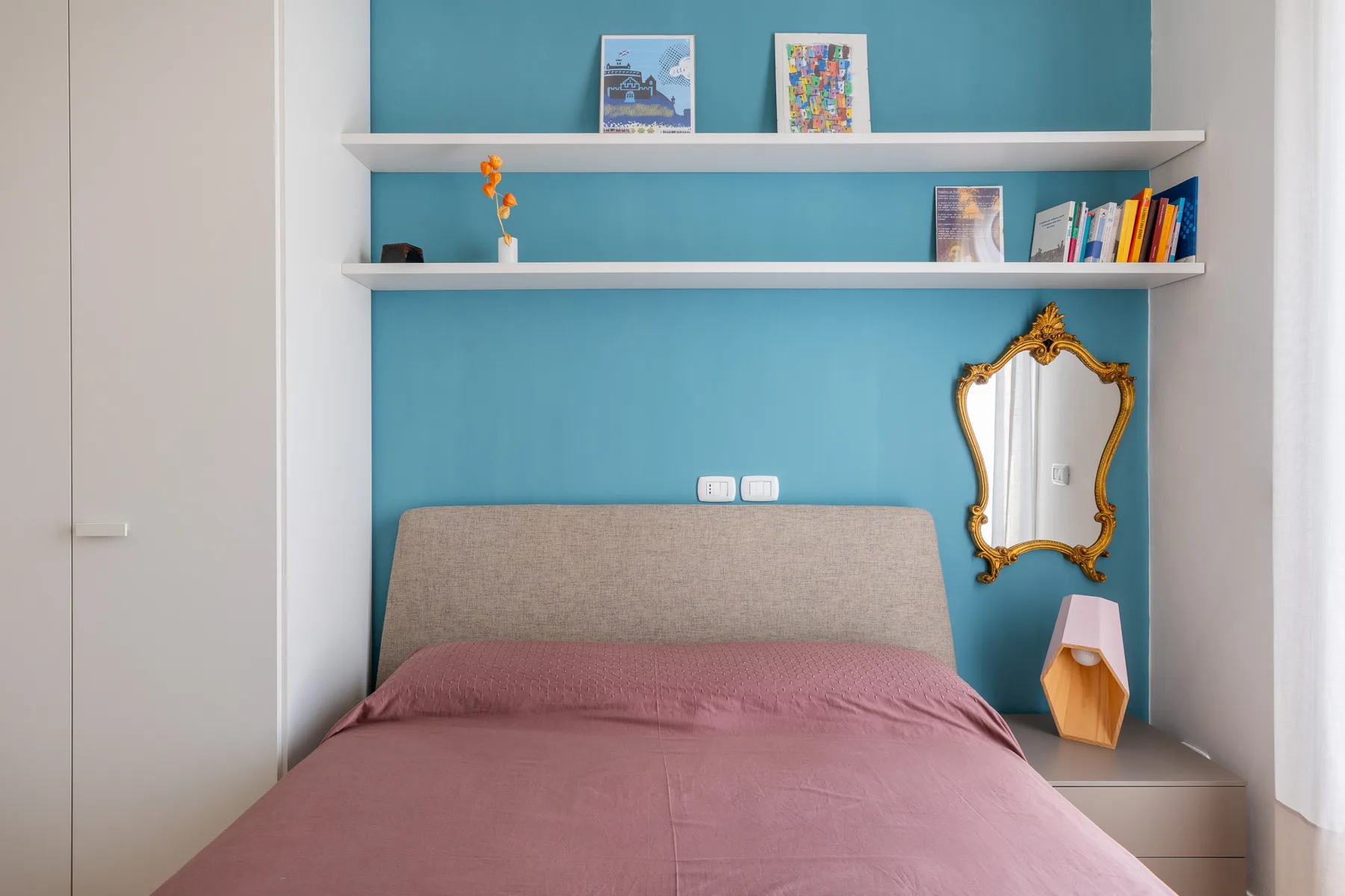 Un dormitorio con una cama frente a una pared turquesa y estantes empotrados.