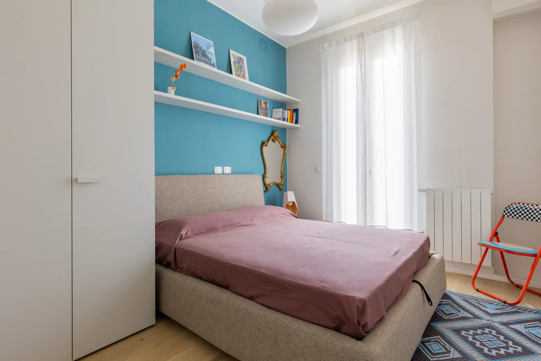 Un dormitorio con una cama, una pared azul y cortinas translúcidas.