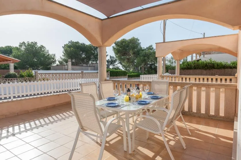 Comedor en un patio embaldosado, con una mesa puesta bajo una terraza cubierta.