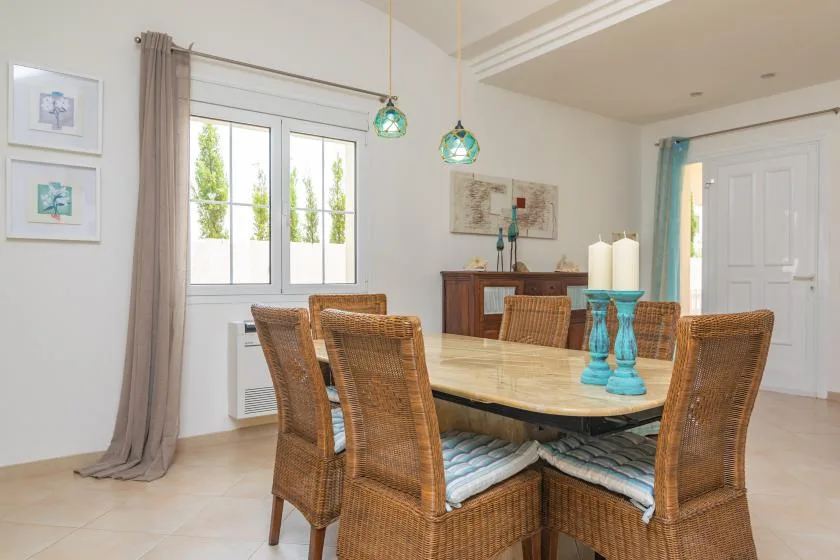 Un comedor con una mesa de madera, asientos tejidos y lámparas colgantes.