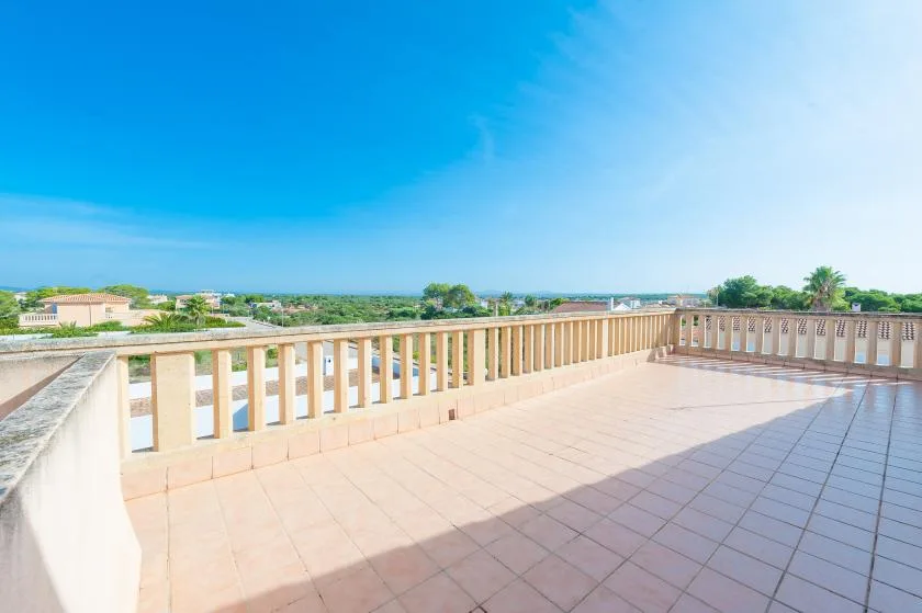 Una terraza exterior embaldosada con barandilla ofrece vistas a edificios y vegetación cercanos.