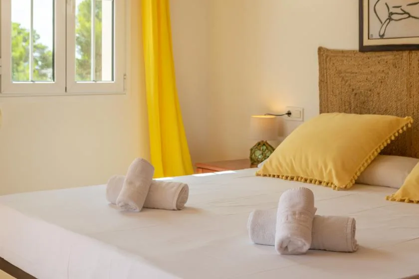 Un dormitorio con una cama arreglada, cortinas amarillas y una ventana.