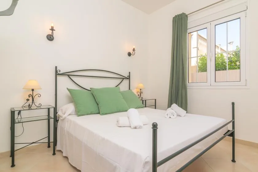 Dormitorio con una cama metálica, almohadas verdes y una ventana con cortinas verdes.