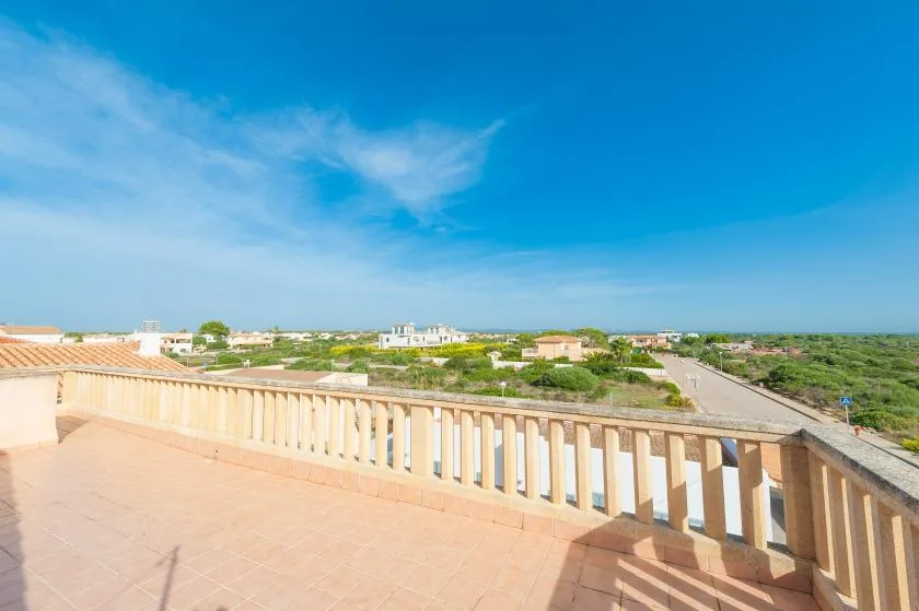 Una terraza soleada ofrece vistas de edificios bajos, vegetación y una carretera bajo un cielo azul.