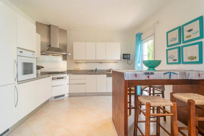 Una cocina luminosa con gabinetes blancos, horno y barra de desayuno de madera.