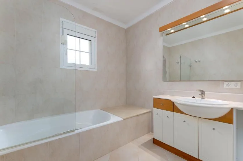 Un baño alicatado con bañera, lavabo con mueble y espejo de pared.