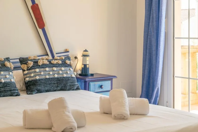 Un dormitorio con una cama, cojines estampados y cortinas azules junto a una ventana luminosa.