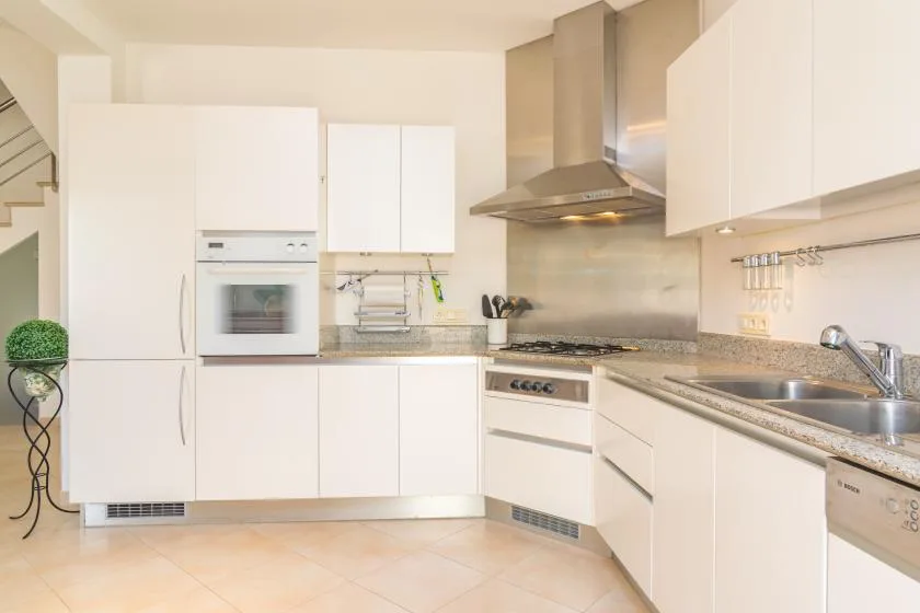 Una cocina luminosa con gabinetes blancos, un horno empotrado y una campana extractora de acero inoxidable.