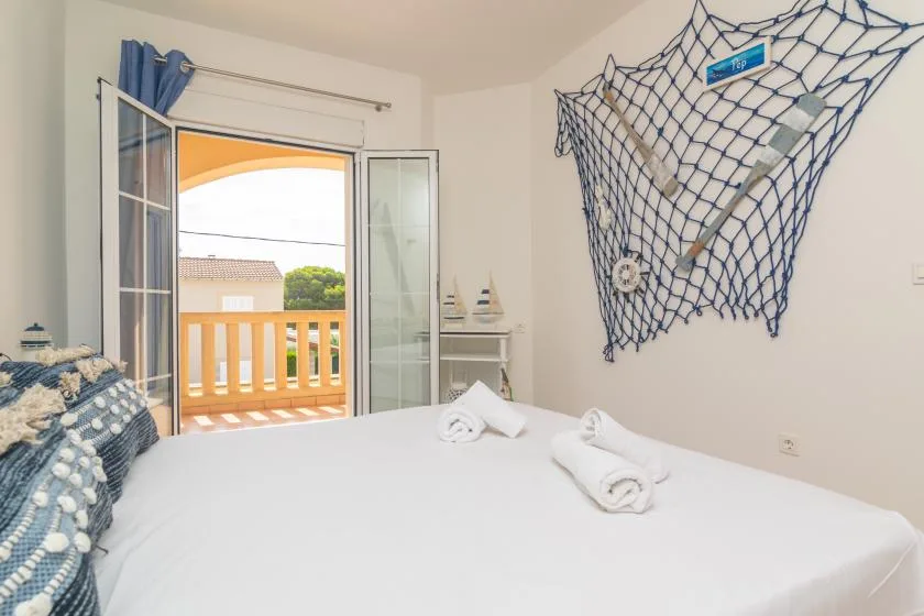 Un dormitorio con una cama blanca junto a una puerta abierta al balcón.