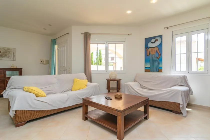 Una sala luminosa tiene asientos alrededor de una mesa de centro de madera junto a varias ventanas.