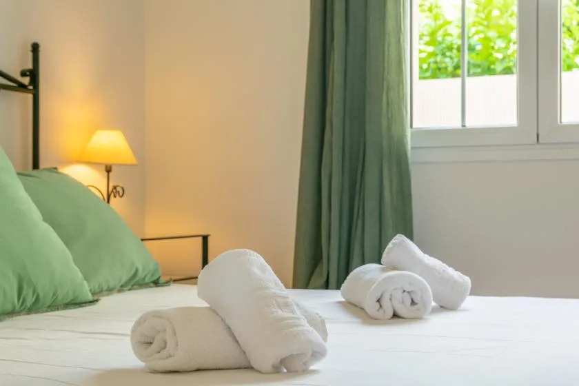 Un dormitorio con una cama bien tendida, toallas dobladas y una ventana.