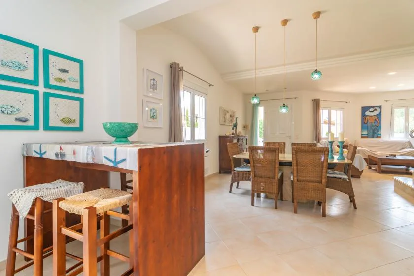 Un comedor luminoso con una mesa larga, asientos tejidos y lámparas colgantes.