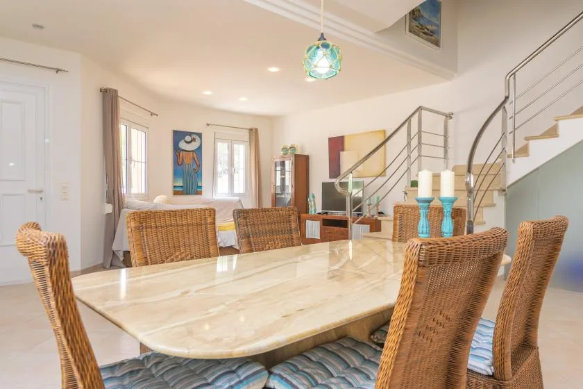 Un comedor luminoso con una mesa larga y una escalera al fondo.