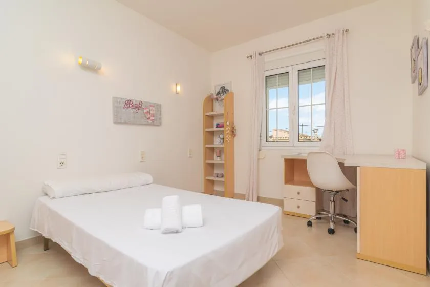 Un dormitorio luminoso con una cama y un escritorio junto a la ventana.