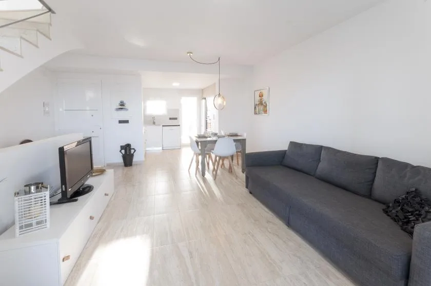 Una sala luminosa con un sofá oscuro y una mesa de comedor junto a la cocina.
