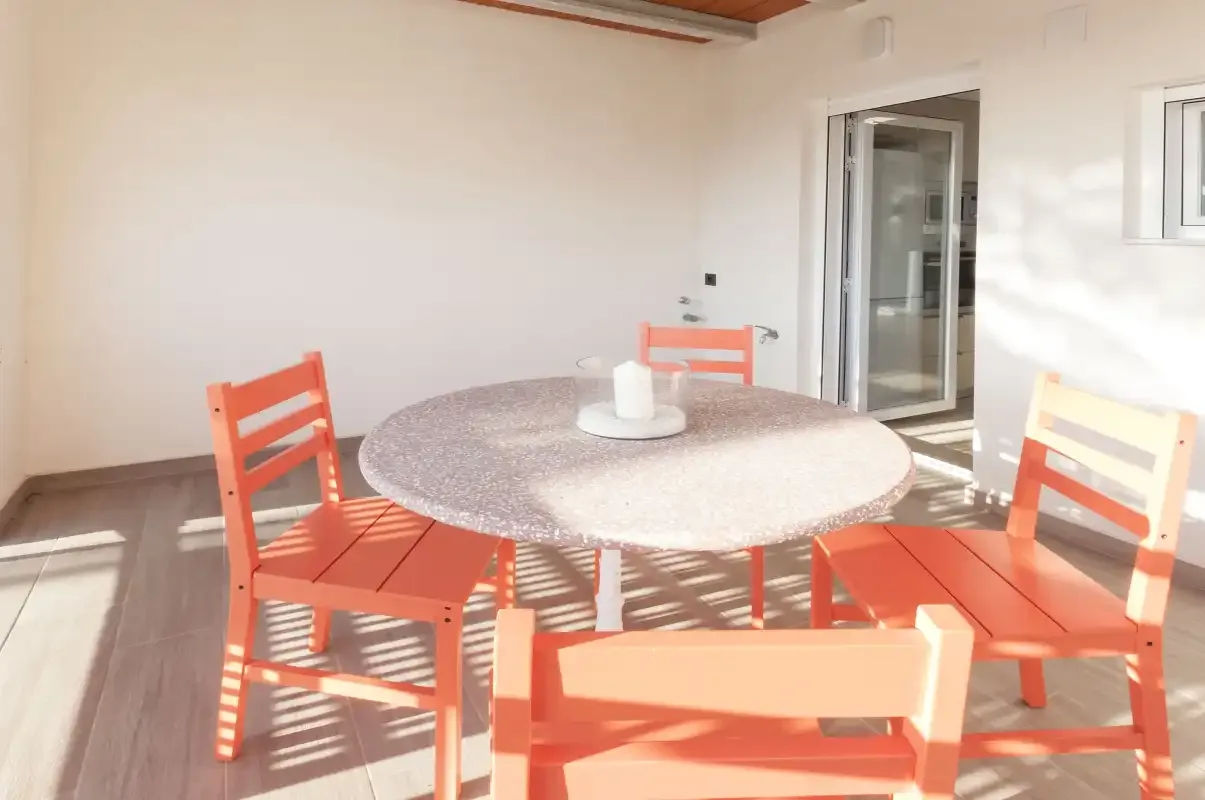 Una luminosa zona de comedor al aire libre con una mesa redonda y asientos naranjas.