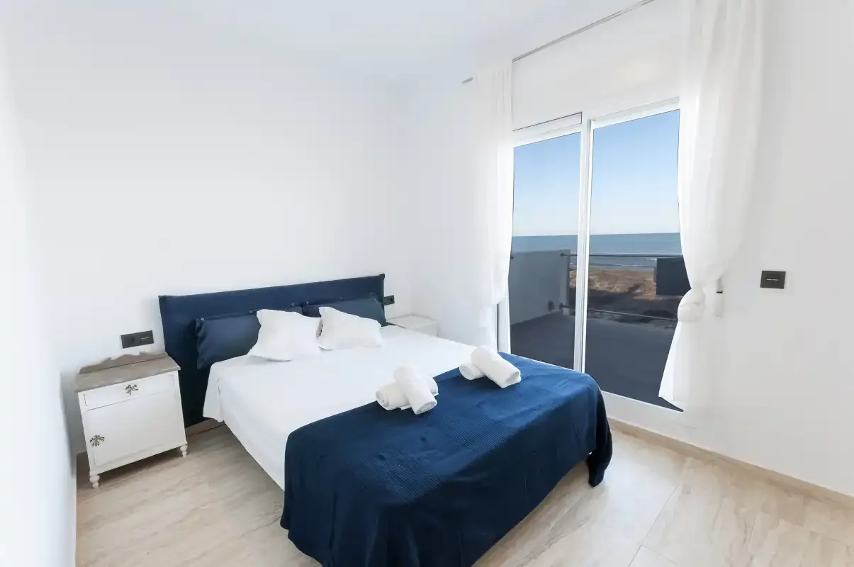Un dormitorio luminoso con una cama y vistas al mar a través de puertas de cristal.