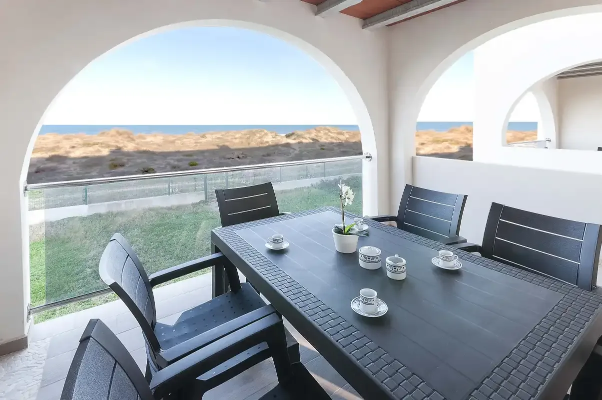 Una zona de comedor exterior cubierta se abre a una vista costera.