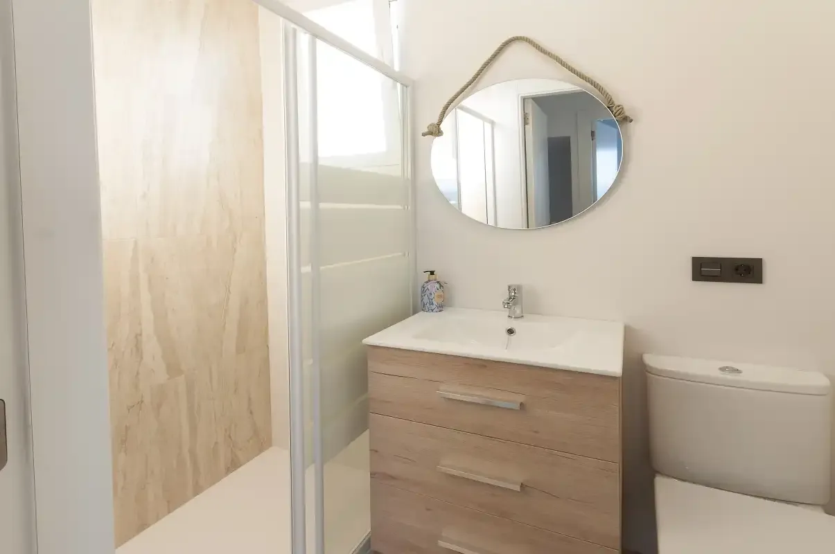 Un baño luminoso con lavabo, espejo, inodoro y ducha de vidrio.