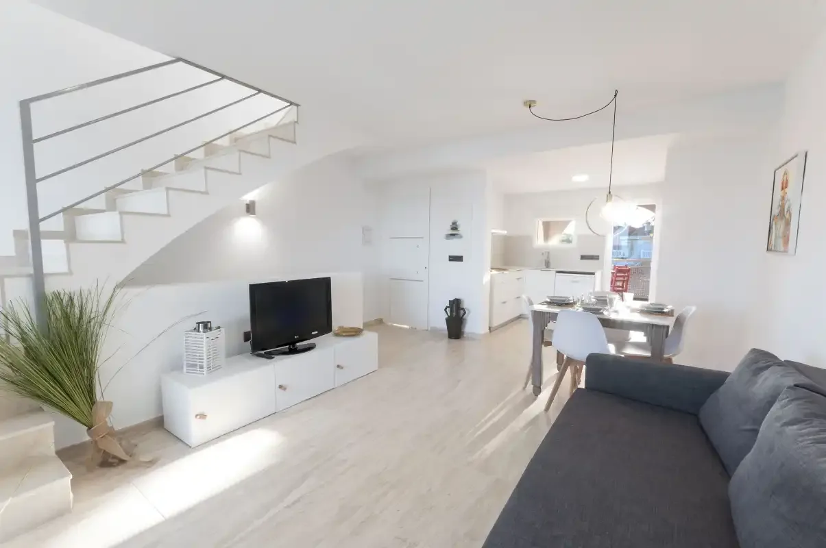 Un salón y cocina diáfanos y luminosos, con televisor y mesa de comedor.