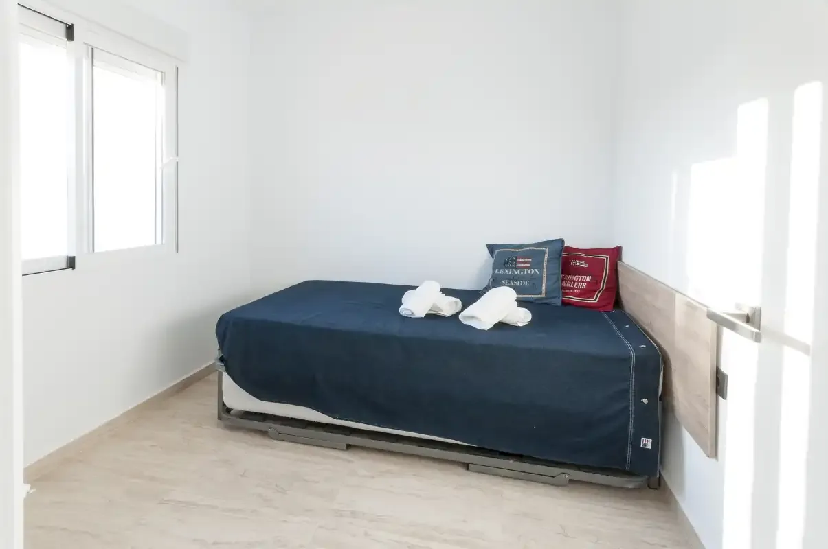 Un dormitorio con una cama cubierta con ropa de cama azul oscuro y dos toallas dobladas.