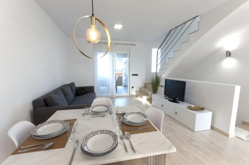 Una luminosa sala de estar y comedor tiene una mesa puesta, asientos y una escalera.