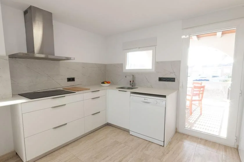 Una cocina luminosa con gabinetes blancos, una placa de cocina y un fregadero.