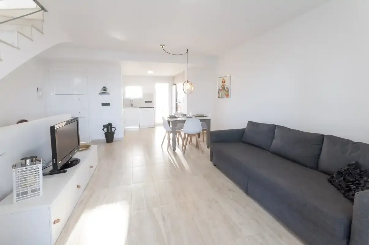 Una luminosa sala de estar y comedor con un televisor y asientos grises.