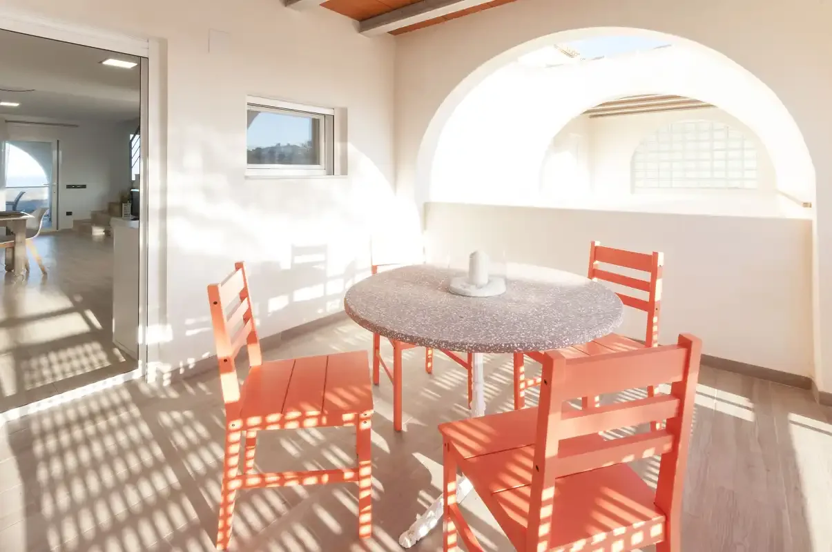 Un comedor luminoso con una mesa redonda y asientos rojos junto a un arco.