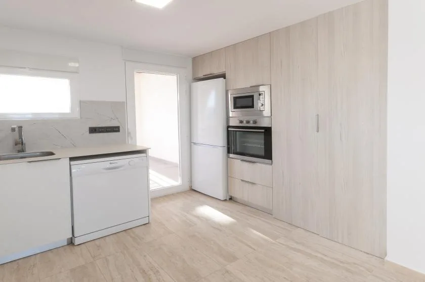 Una cocina luminosa con gabinetes claros, electrodomésticos empotrados y una encimera.