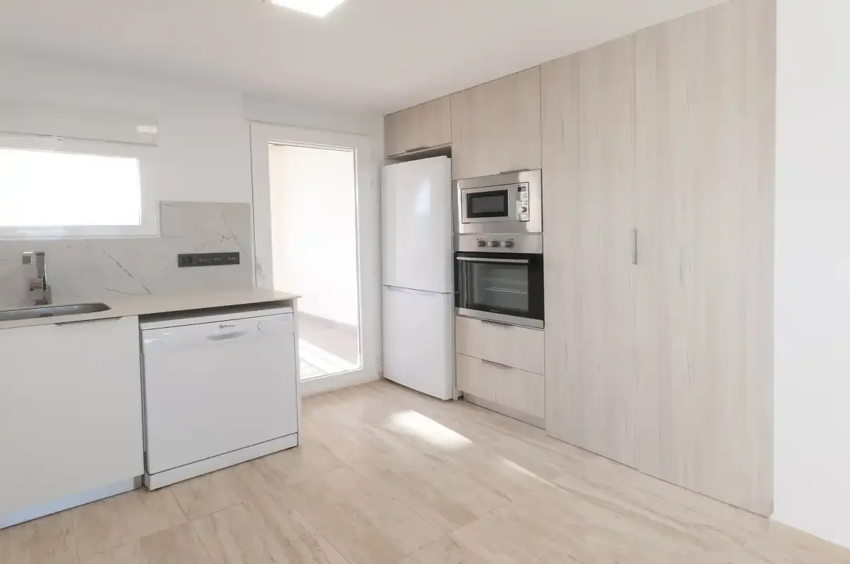 Una cocina luminosa con armarios claros, refrigerador y electrodomésticos integrados.