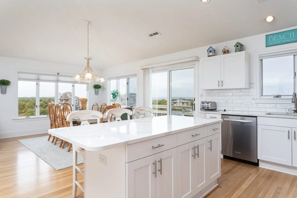 A bright kitchen with a large island and dining area beside broad windows.