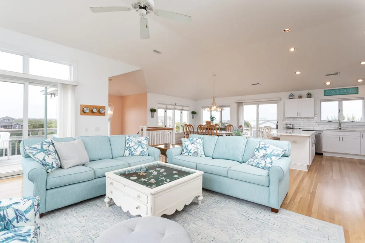 An open-plan living area has pale seating beside a dining table and kitchen.