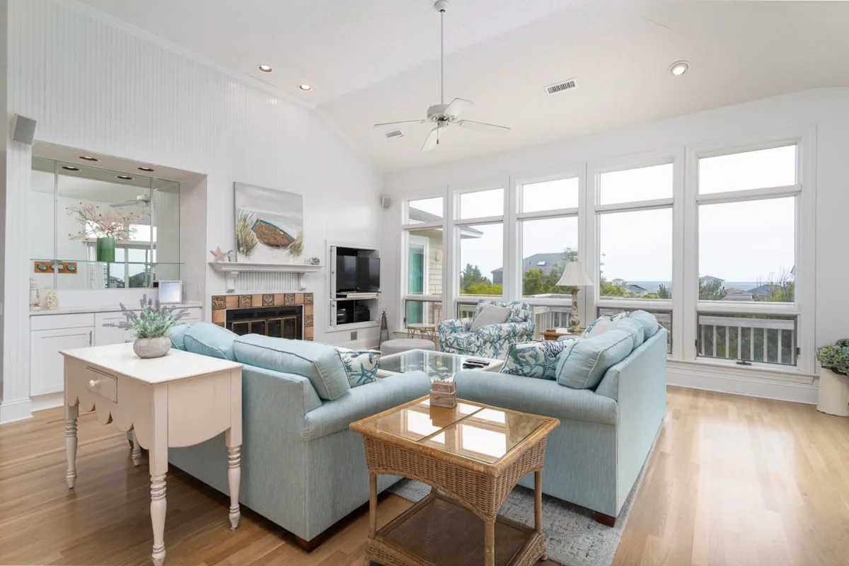 A bright living room with seating arranged around a coffee table and large windows.